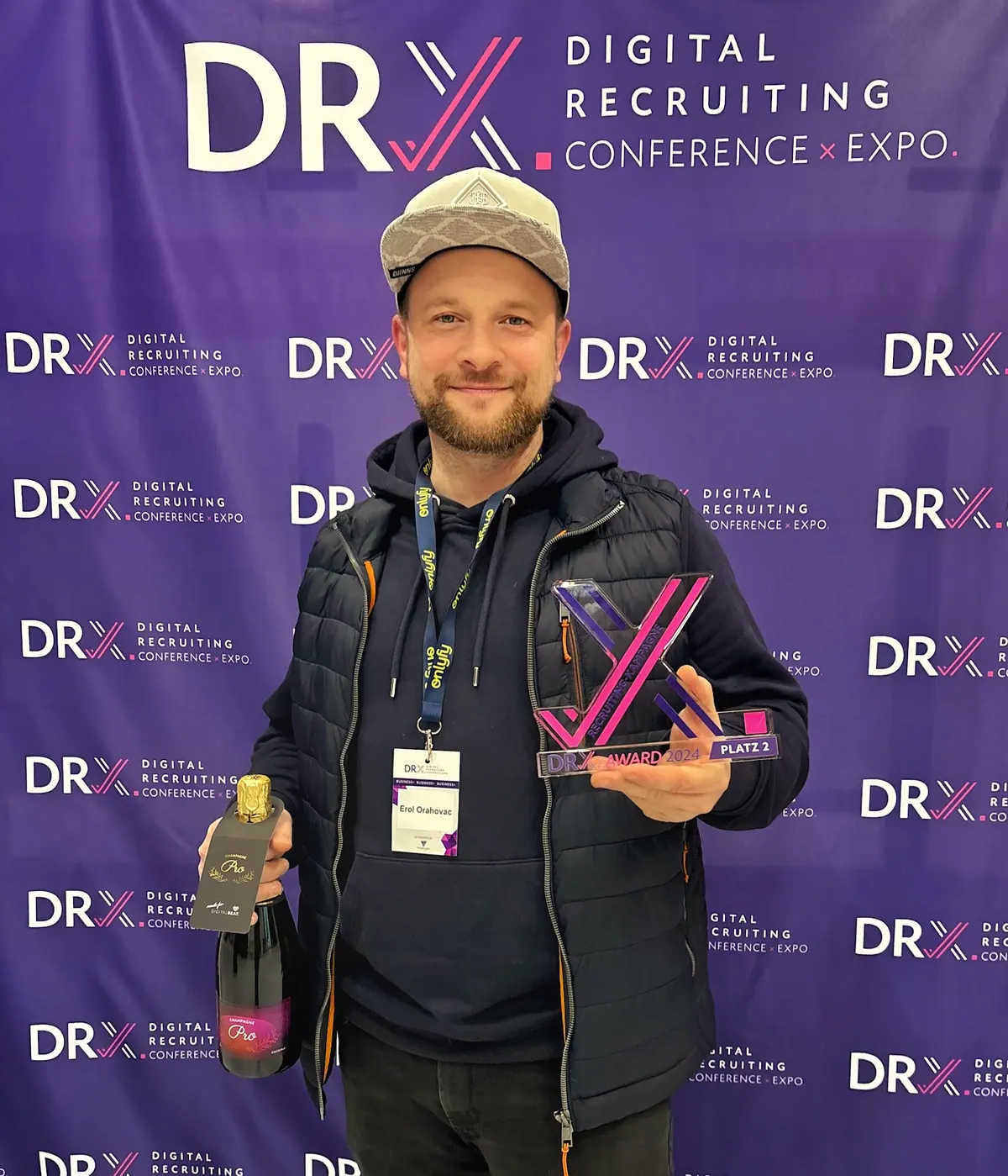 Erol Orahovac mit der Trophäe des DRX Award 2024 (Platz 2, Recruiting-Kampagne) vor der Wand der DRX Digital Recruiting Conference.
